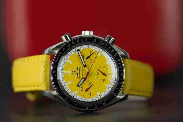 Chronograph mit gelbem Zifferblatt vor rotem Hintergrund